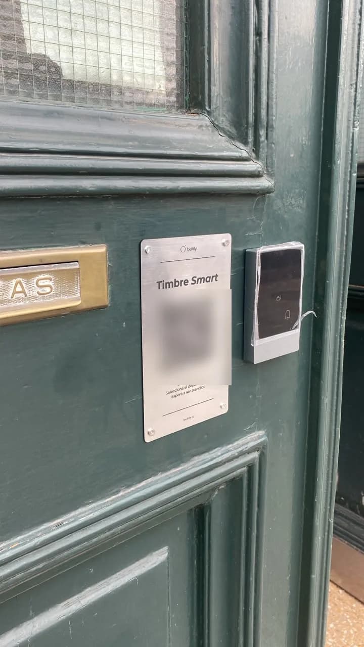 Placa QR de Bellify instalada junto al timbre en la puerta de entrada de un edificio